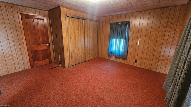 unfurnished bedroom featuring carpet flooring, wood walls, and a closet