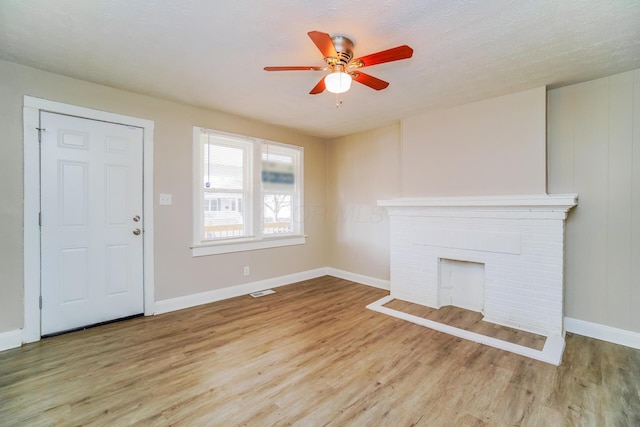 unfurnished living room with a textured ceiling, a fireplace, ceiling fan, and light wood-type flooring