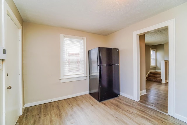 kitchen with black refrigerator, a textured ceiling, and light hardwood / wood-style flooring