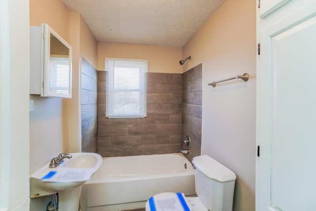 bathroom with tiled shower / bath combo, a textured ceiling, and toilet