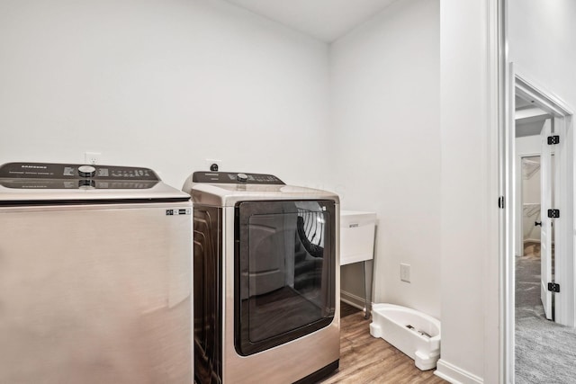 laundry room with washing machine and clothes dryer and light hardwood / wood-style flooring