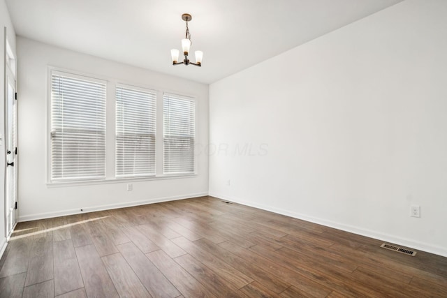 empty room with dark hardwood / wood-style floors, a healthy amount of sunlight, and an inviting chandelier