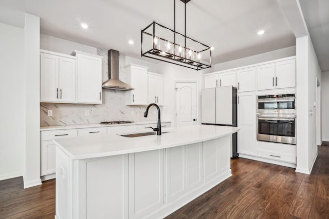 kitchen featuring sink, white cabinets, wall chimney range hood, and a center island with sink