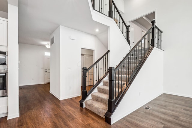 staircase featuring a towering ceiling and hardwood / wood-style flooring