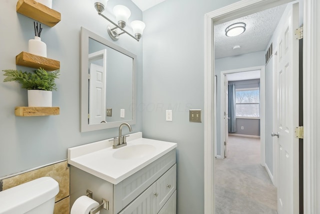 bathroom with a textured ceiling, vanity, and toilet