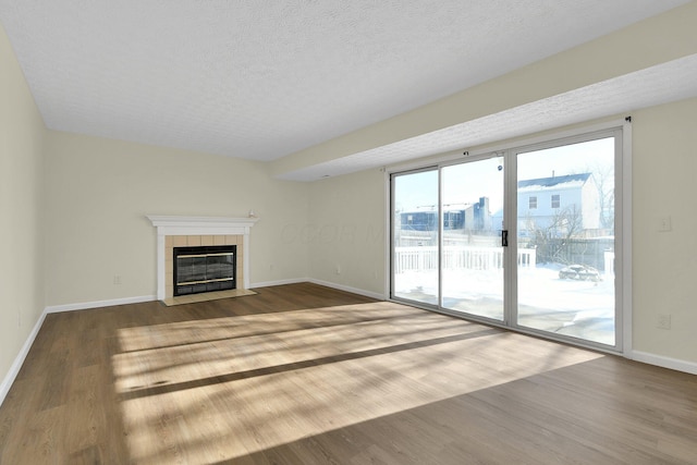 unfurnished living room with hardwood / wood-style floors, a textured ceiling, and a tiled fireplace