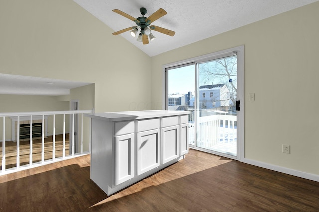 interior space with ceiling fan, a kitchen island, hardwood / wood-style floors, vaulted ceiling, and white cabinets