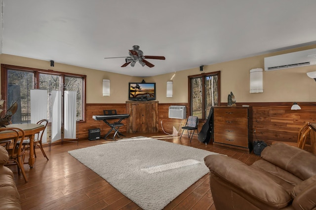 living room with an AC wall unit, ceiling fan, wooden walls, and hardwood / wood-style flooring