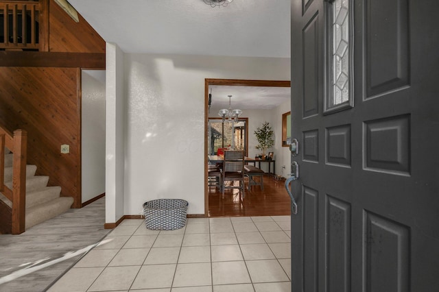 tiled foyer with wood walls and an inviting chandelier