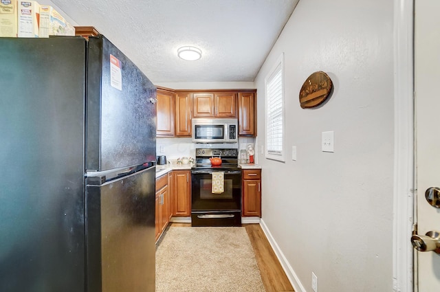 kitchen with black appliances, a textured ceiling, and light hardwood / wood-style floors