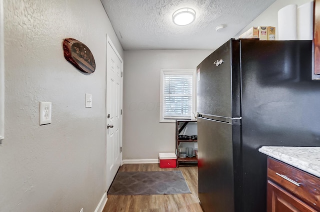 kitchen with black refrigerator, a textured ceiling, and light wood-type flooring