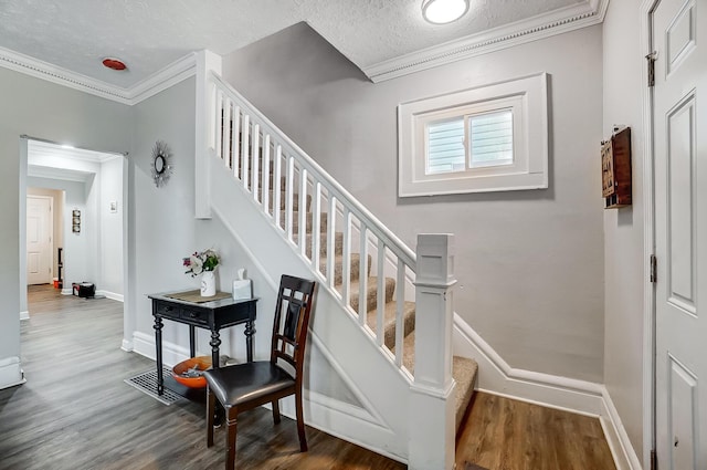 staircase featuring wood-type flooring, a textured ceiling, and ornamental molding