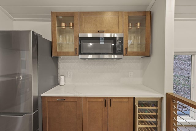 kitchen featuring decorative backsplash, light stone counters, stainless steel appliances, and beverage cooler