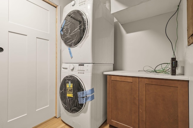 laundry room featuring cabinets, stacked washing maching and dryer, and light wood-type flooring