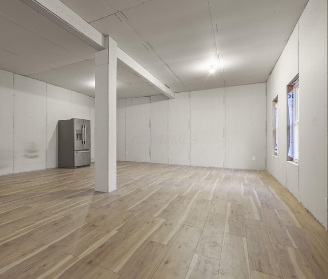 basement featuring stainless steel fridge with ice dispenser and light wood-type flooring