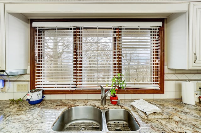 kitchen featuring white cabinets, decorative backsplash, light stone countertops, and sink