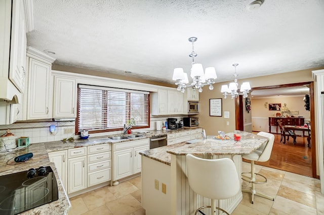 kitchen with a kitchen breakfast bar, stainless steel appliances, sink, a notable chandelier, and a kitchen island