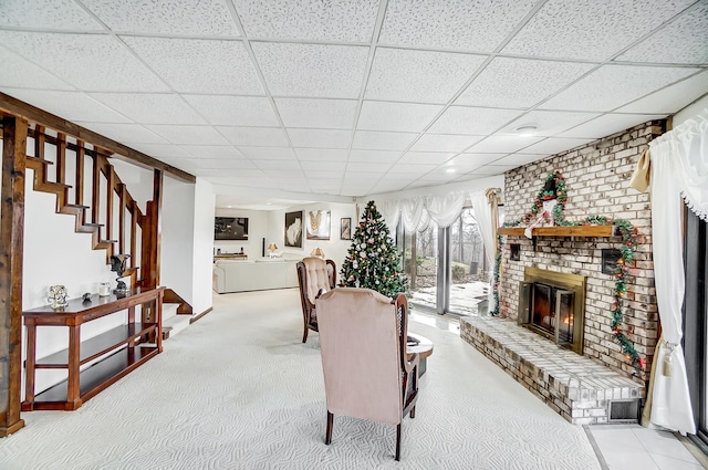 living room featuring a fireplace, light colored carpet, and a drop ceiling