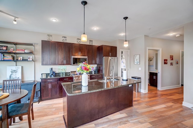 kitchen with dark stone counters, pendant lighting, a center island with sink, and stainless steel appliances