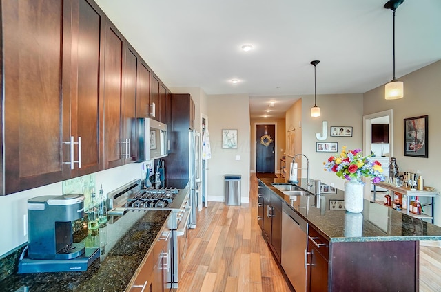 kitchen with sink, dark stone countertops, pendant lighting, a center island with sink, and appliances with stainless steel finishes