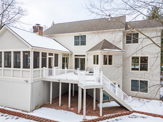 snow covered house featuring a wooden deck and a sunroom