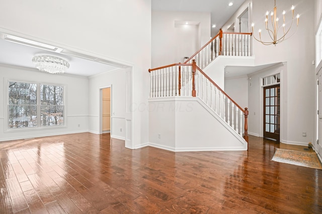 unfurnished living room featuring a high ceiling, ornamental molding, a notable chandelier, and dark hardwood / wood-style flooring