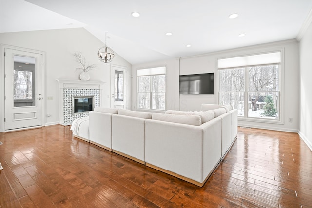 unfurnished living room with lofted ceiling, a tiled fireplace, ornamental molding, hardwood / wood-style flooring, and a notable chandelier