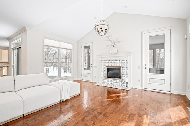 unfurnished living room with vaulted ceiling, a chandelier, a tiled fireplace, and hardwood / wood-style floors