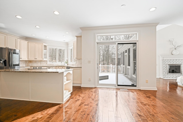 kitchen featuring stainless steel fridge, stone counters, backsplash, a fireplace, and light wood-type flooring