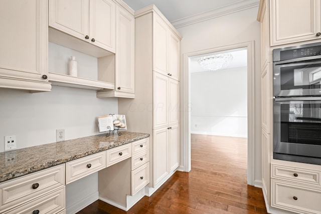 kitchen featuring built in desk, ornamental molding, dark hardwood / wood-style floors, double oven, and stone counters