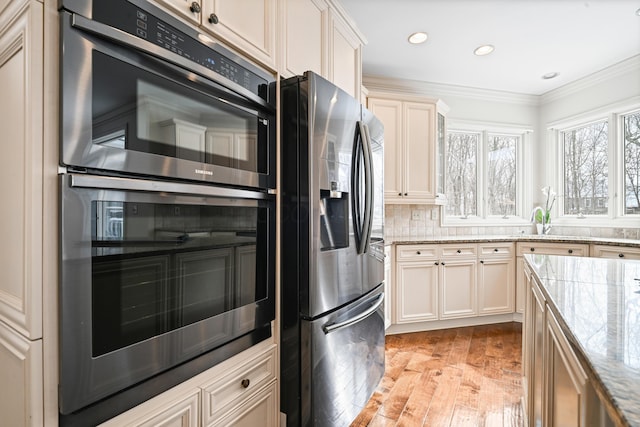 kitchen with stainless steel refrigerator with ice dispenser, crown molding, light hardwood / wood-style flooring, double wall oven, and cream cabinets