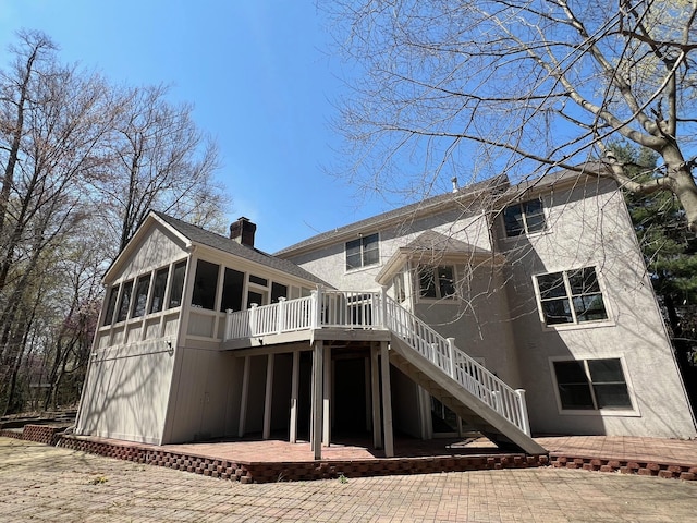 rear view of house featuring a chimney, a deck, a sunroom, a patio, and stairs