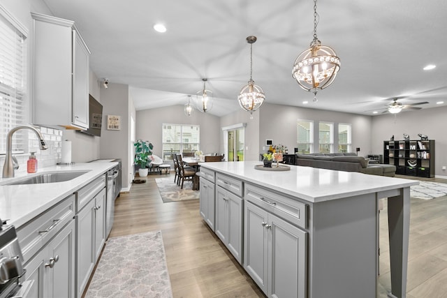 kitchen featuring stainless steel dishwasher, ceiling fan with notable chandelier, sink, a kitchen island, and hanging light fixtures