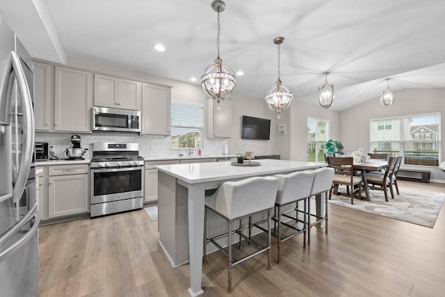 kitchen featuring lofted ceiling, gray cabinets, decorative light fixtures, a kitchen island, and stainless steel appliances