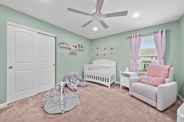 carpeted bedroom with ceiling fan, a closet, and a nursery area