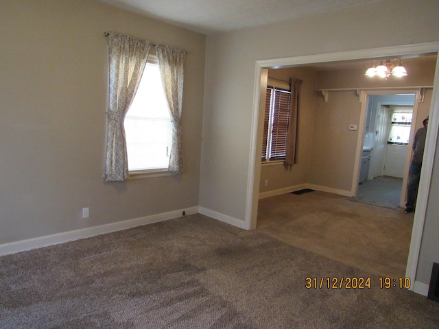 carpeted empty room with plenty of natural light and a notable chandelier