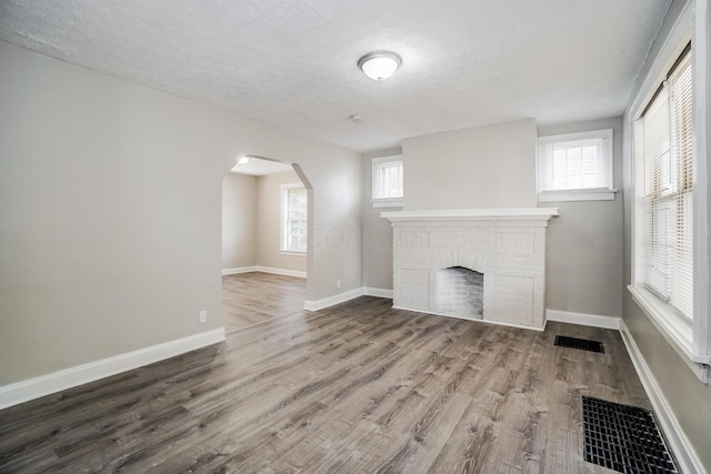 unfurnished living room with a textured ceiling, hardwood / wood-style flooring, a brick fireplace, and a wealth of natural light