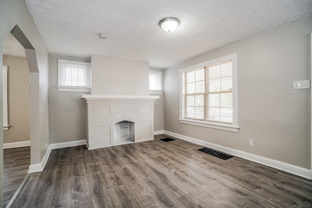 unfurnished living room featuring a textured ceiling, dark hardwood / wood-style floors, and a brick fireplace