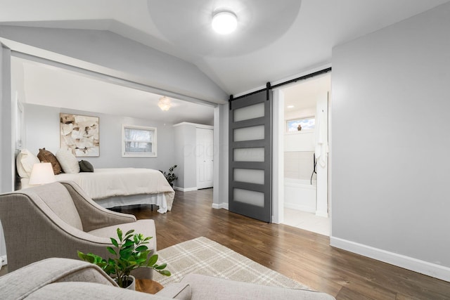 bedroom featuring connected bathroom, a barn door, dark wood-type flooring, and vaulted ceiling