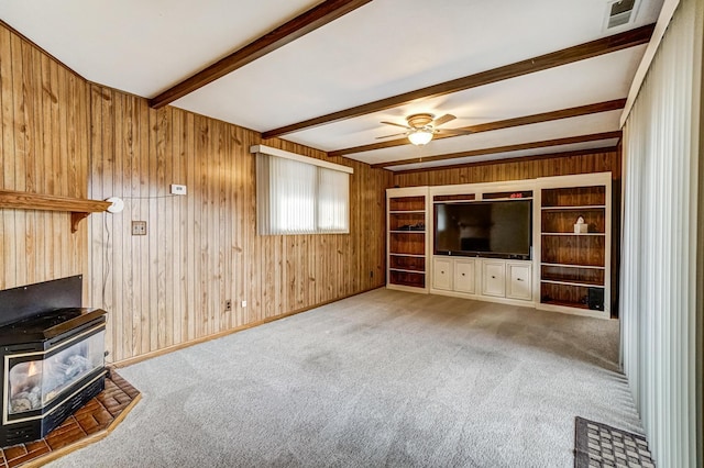 unfurnished living room featuring ceiling fan, beam ceiling, a wood stove, and light carpet