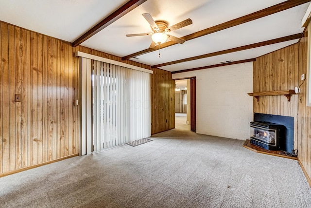 unfurnished living room featuring beam ceiling, a wood stove, ceiling fan, light carpet, and wooden walls