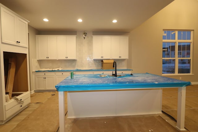 kitchen with backsplash, sink, an island with sink, and white cabinets