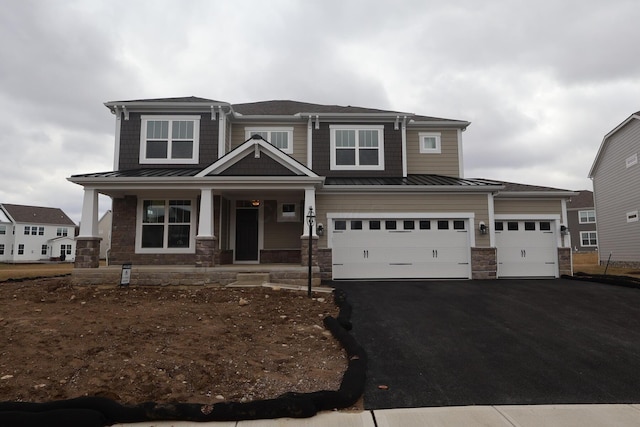 view of front of house featuring driveway, a standing seam roof, stone siding, covered porch, and metal roof