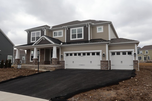 view of front facade featuring a standing seam roof, covered porch, stone siding, aphalt driveway, and metal roof