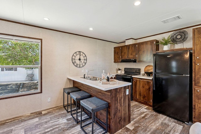 kitchen with a breakfast bar, light wood-type flooring, ornamental molding, and black appliances