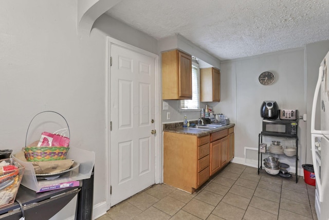 kitchen with a textured ceiling, white refrigerator, light tile patterned floors, and sink