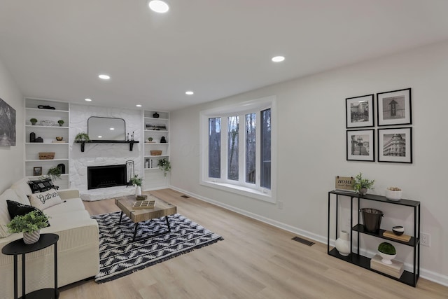 living room with a large fireplace, light hardwood / wood-style floors, and built in features