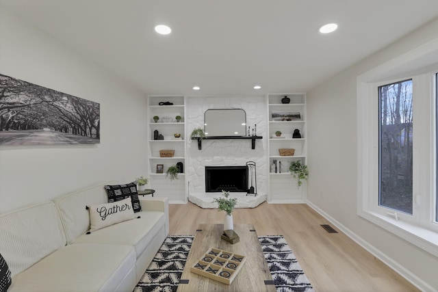 living room with built in shelves, a fireplace, and light hardwood / wood-style floors