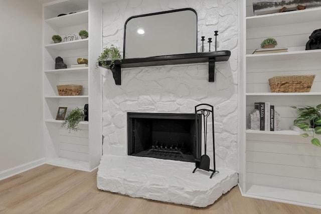 details with hardwood / wood-style flooring, built in shelves, and a stone fireplace