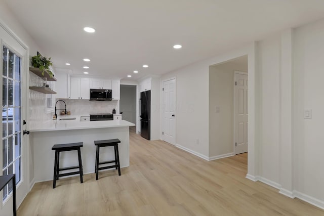 kitchen featuring black appliances, a kitchen breakfast bar, kitchen peninsula, sink, and white cabinetry